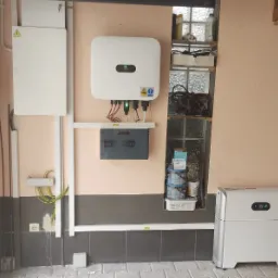 Instalacja z białym falownikiem i magazynem energii Huawei, widoczne kable, bezpieczniki i elementy montażowe na różowej ścianie w garażu z oknem z luksferami.