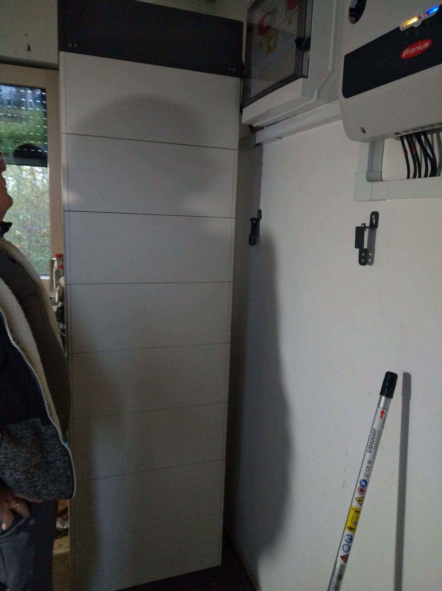 Wnętrze z zainstalowanym magazynem energii, falownikiem Fronius i widocznym fragmentem osoby obserwującej instalację.