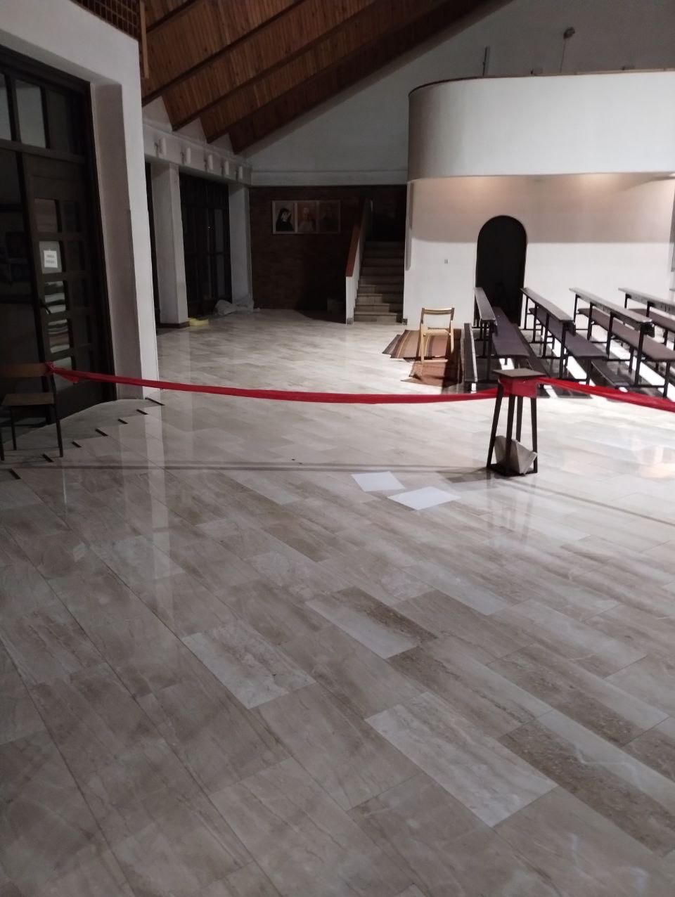 Jasne, marmurkowe płytki podłogowe ułożone w kościele, zabezpieczone czerwoną taśmą, z widocznymi ławkami i schodami w tle.