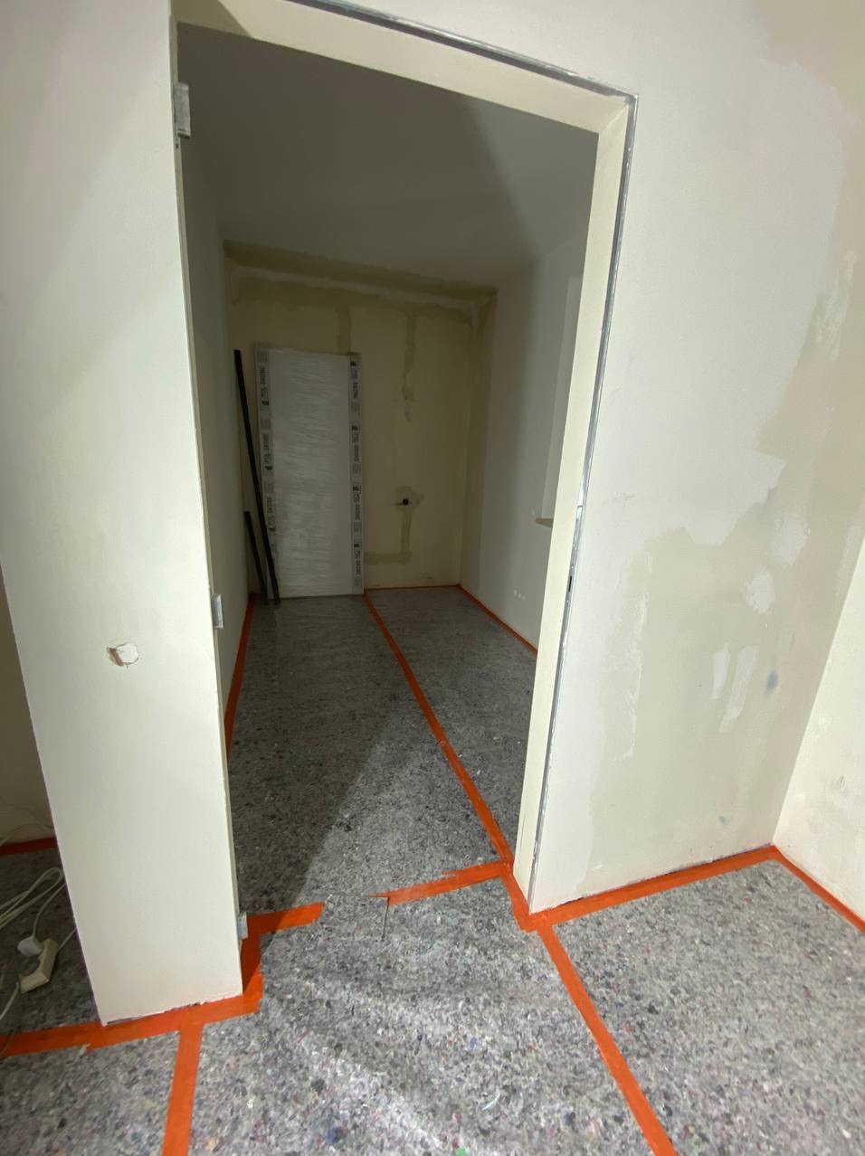 Przygotowanie do prac wykończeniowych: pomieszczenie zabezpieczone folią i taśmą malarską, ściany częściowo wyszpachlowane, widoczne ślady po instalacjach.