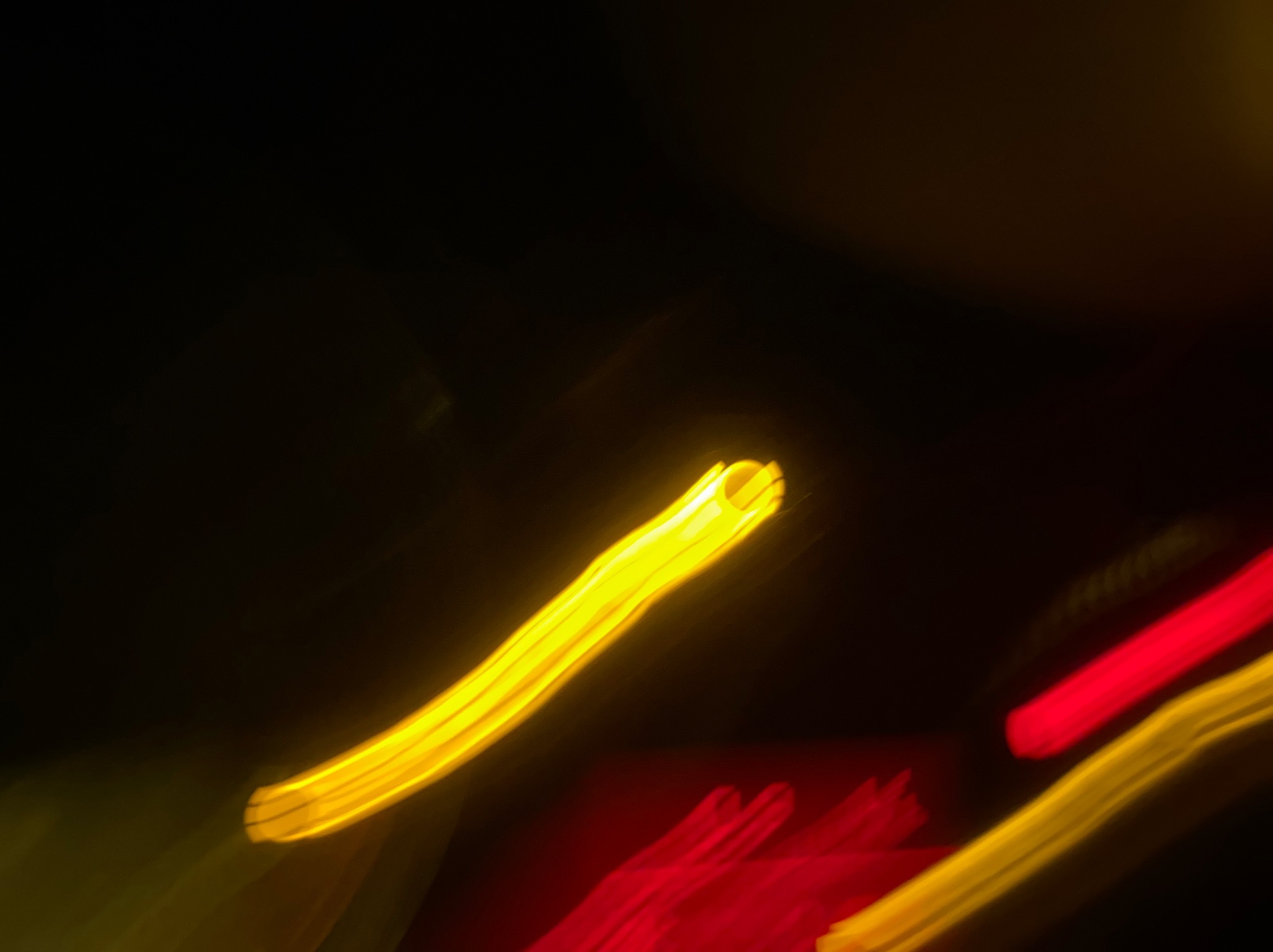 Rozmazane, abstrakcyjne ujęcie świateł w kolorach żółtym i czerwonym na ciemnym tle, przypominające efekt malowania światłem.