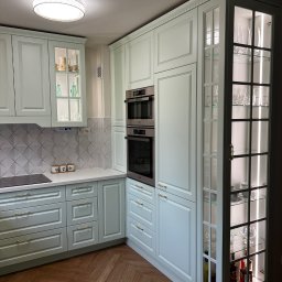 ACTUAL - Jasna, pastelowa kuchnia na wymiar z drewnianą podłogą w jodełkę, przeszklone szafki z podświetleniem LED eksponujące szkło i butelki, zabudowane piekarniki.