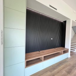 ACTUAL - Nowoczesna zabudowa ściany telewizyjnej z pionowymi panelami dekoracyjnymi, szafką RTV z drewnianym blatem i szafką boczną w kolorze miętowym, na podłodze panele drewnopodobne.