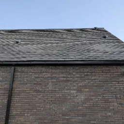 Nowoczesny dom z ciemnobrązową ceglaną elewacją i dachem pokrytym szarą dachówką ceramiczną z trzema kominkami wentylacyjnymi.