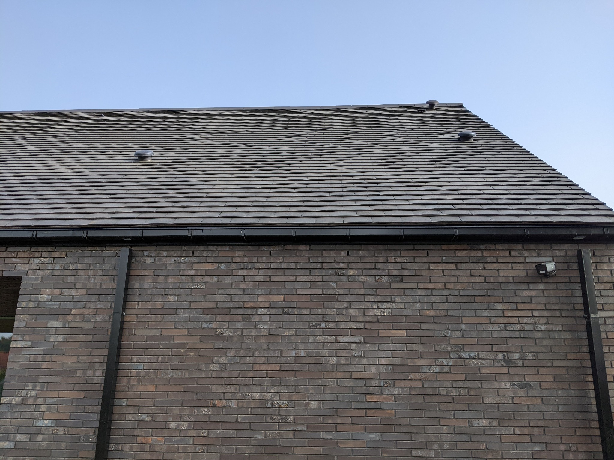 Nowoczesny dom z ciemnobrązową ceglaną elewacją i dachem pokrytym szarą dachówką ceramiczną z trzema kominkami wentylacyjnymi.