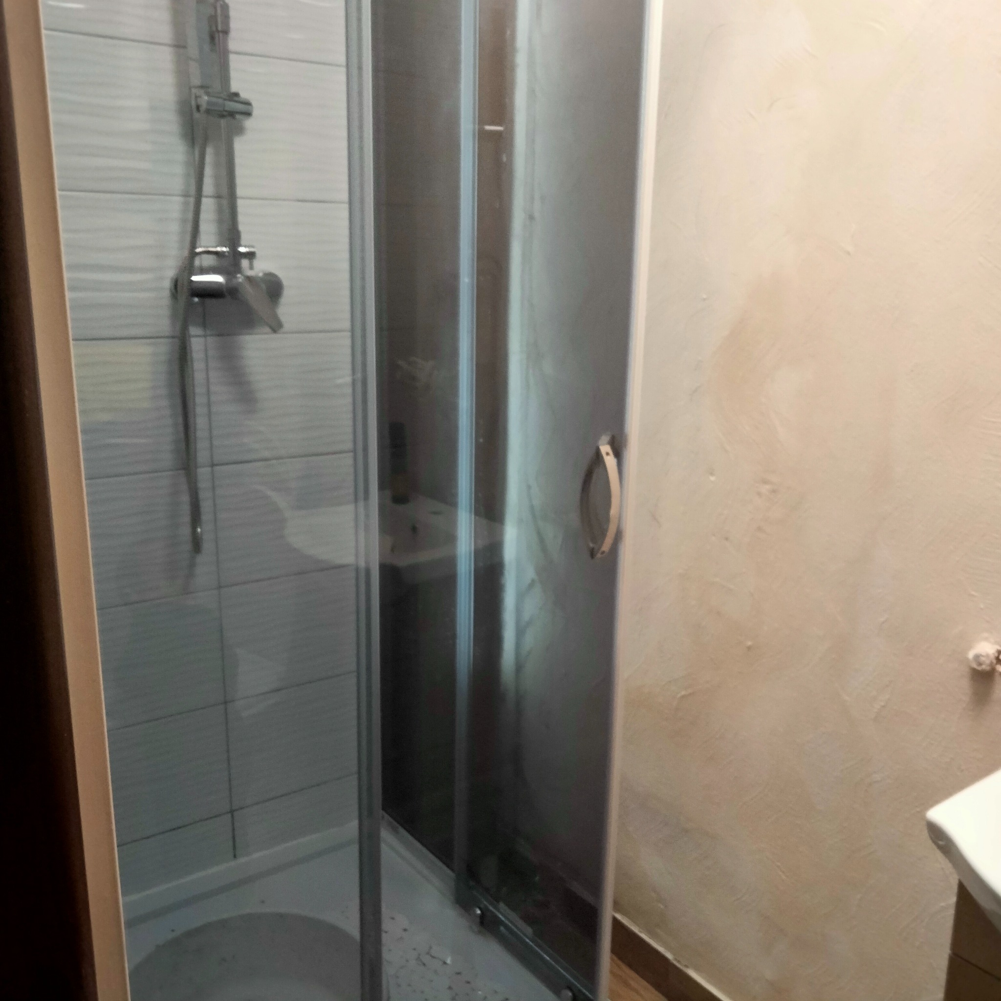 Zamknięta kabina prysznicowa z chromowaną armaturą, widoczna na tle ściany wykończonej beżowym tynkiem w Otwocku.