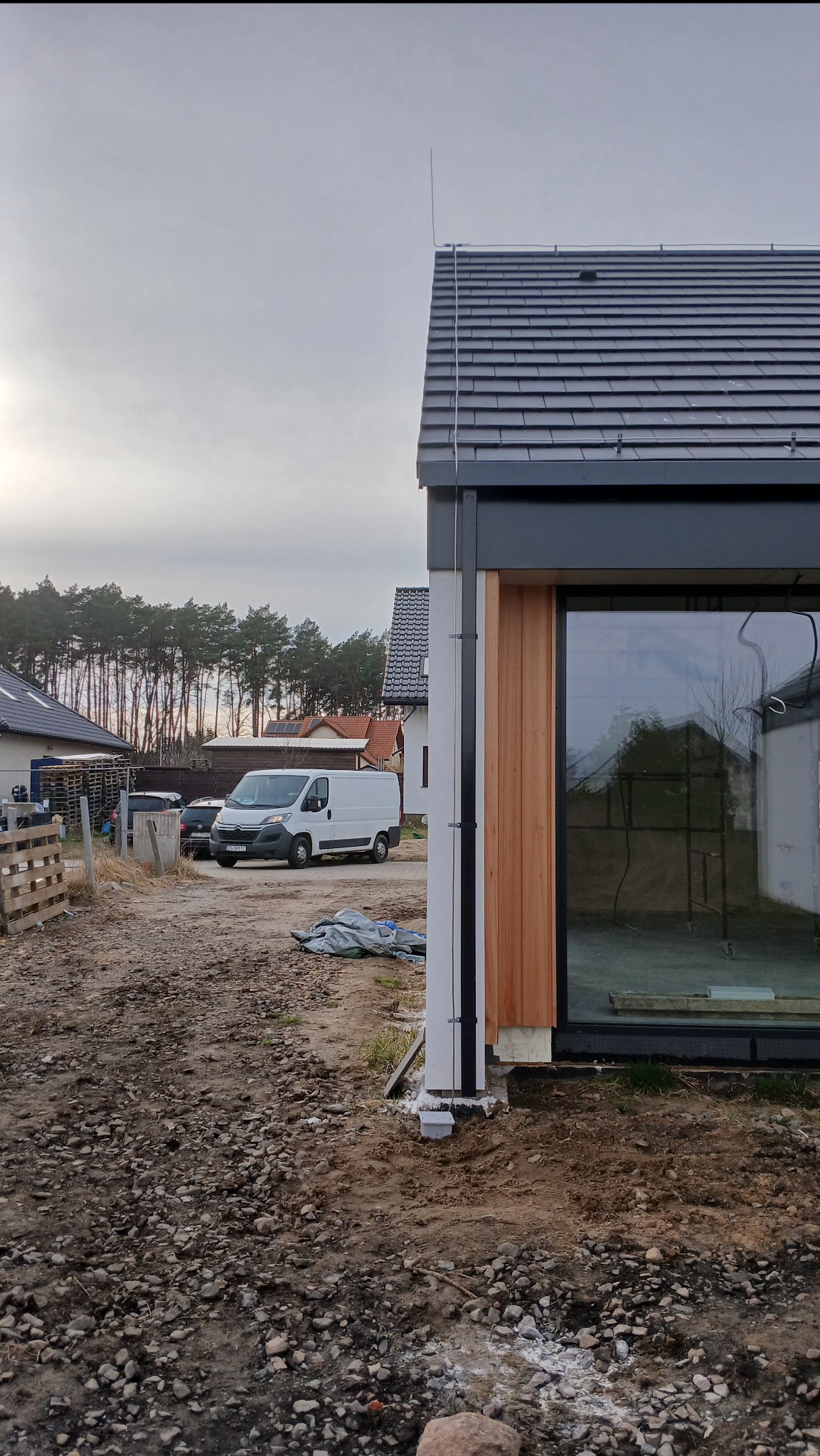 Nowoczesny dom jednorodzinny w trakcie wykończenia z zainstalowaną instalacją odgromową, widoczny przewód odprowadzający na elewacji i zwód pionowy na dachu, na pierwszym planie gruz i ziemia.