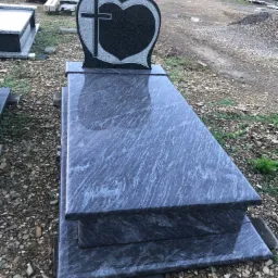 Granitowy pomnik z sercem i krzyżem, widoczne szlifowane krawędzie i polerowana powierzchnia, na tle placu z kamieniami.