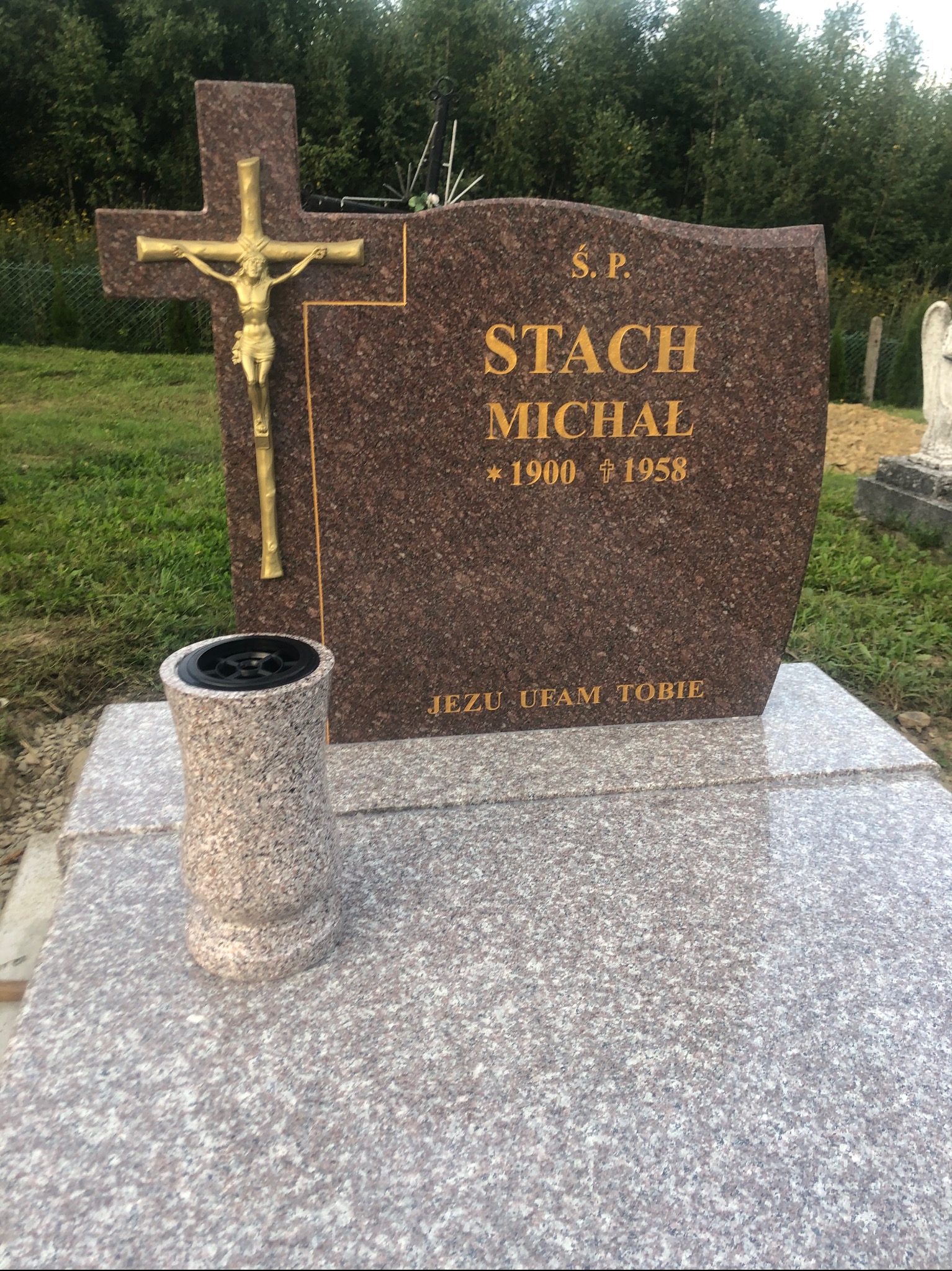 Granitowy pomnik z krzyżem i wazonem na kwiaty, z wygrawerowanymi złotymi literami imienia i nazwiska oraz datami urodzin i śmierci.