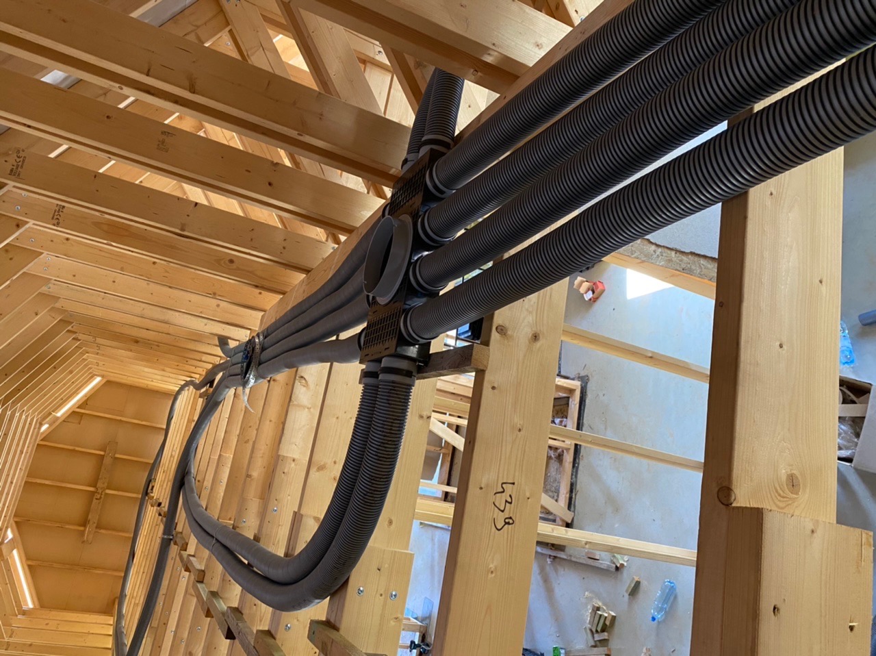 Szare, karbowane rury wentylacyjne zamontowane w drewnianej konstrukcji dachu poddasza w trakcie budowy.