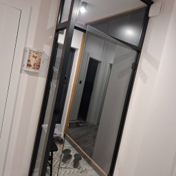 Rafał Graczyk Rafmont - Szklane drzwi wewnętrzne z czarną ramą, widok na korytarz. Minimalistyczny design, jasne ściany, dekoracja ścienna. Nowoczesne wykończenie wnętrza.