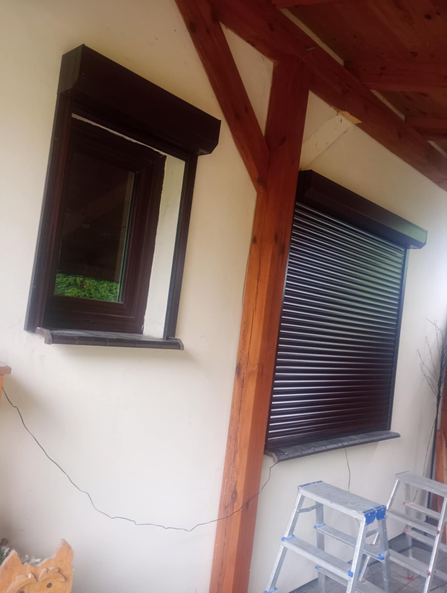 Brązowe rolety zewnętrzne na oknach budynku z drewnianą konstrukcją dachu. Widoczne drabiny malarskie.