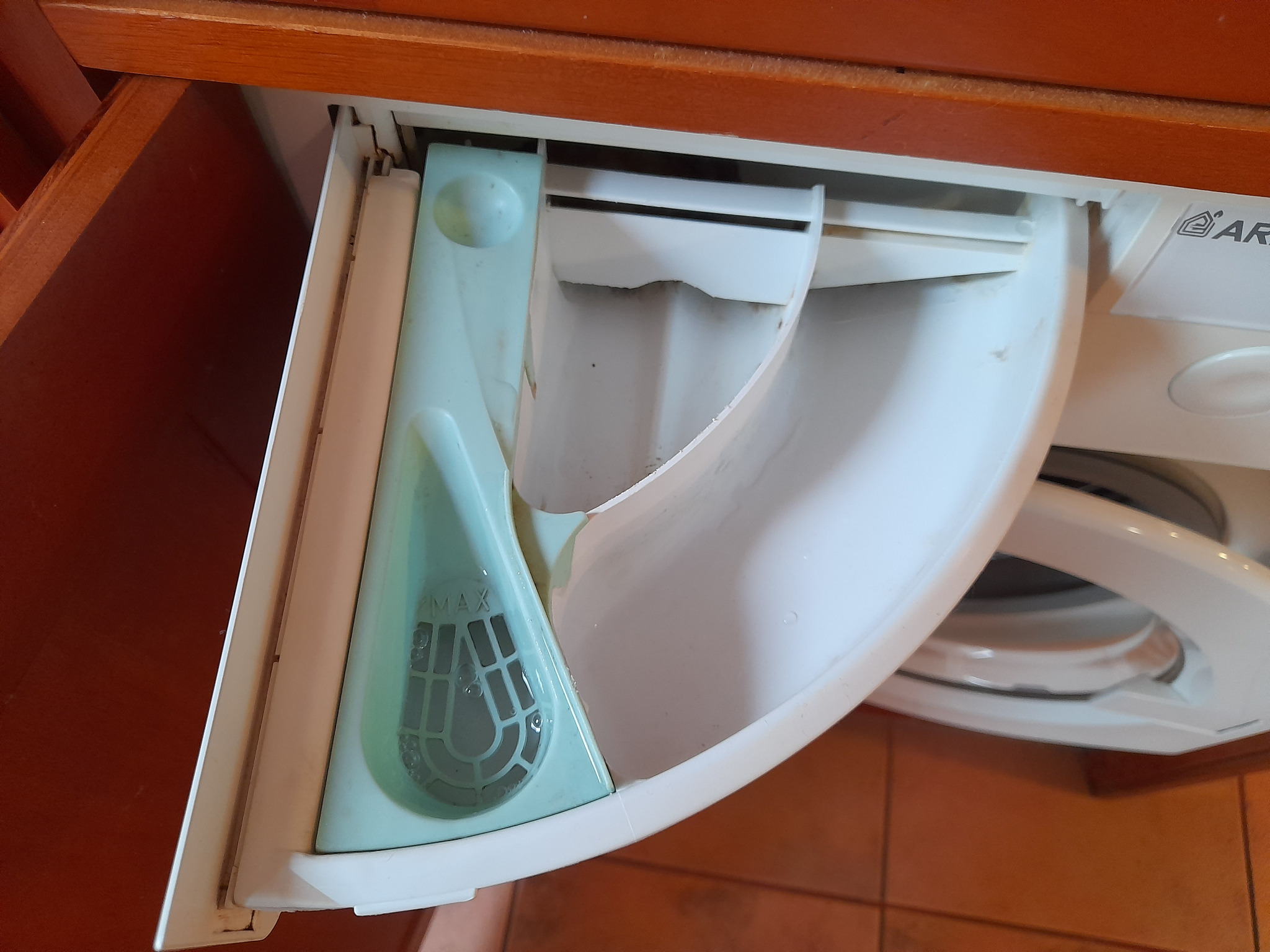Szczegółowe ujęcie otwartej szuflady na detergent w pralce Ariston, ukazujące osady i zabrudzenia. Widoczny wskaźnik MAX.