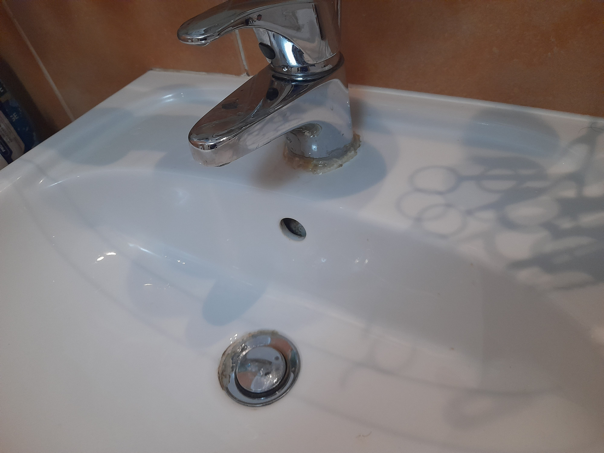 Zlew z osadem kamiennym wokół kranu i odpływu. Widoczne zacieki i brud. Potrzeba sprzątania i usunięcia osadów. Ujęcie z góry, bliski kadr.