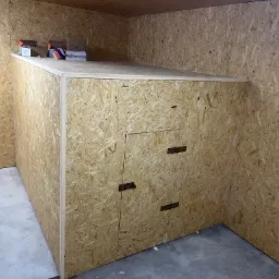 Poddasze wykończone płytami OSB, widoczna zabudowa z drzwiczkami i gniazdko elektryczne na ścianie.