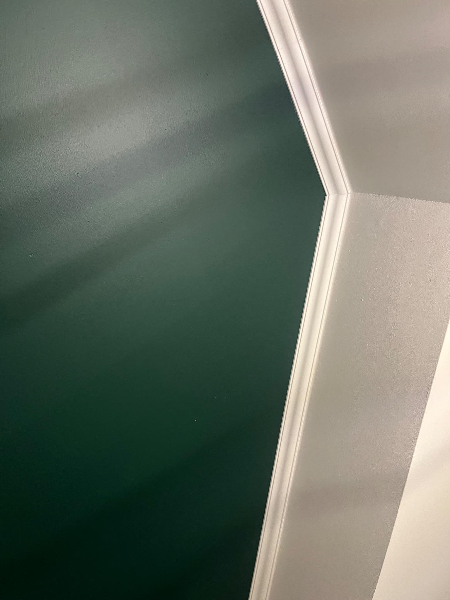 Fragment ściany pomalowanej na ciemnozielono, stykającej się z sufitem w kolorze jasnoszarym, oddzielone białą listwą dekoracyjną.