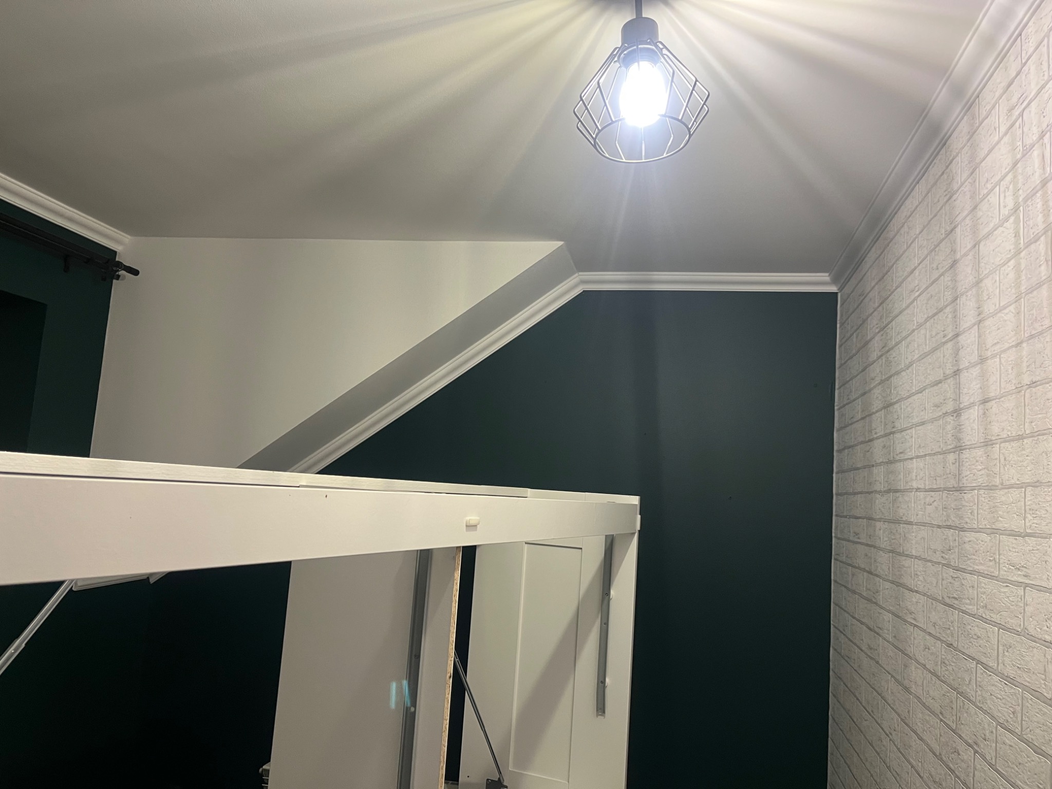 Poddasze z oświetleniem, ściana pomalowana na ciemnozielono, fragment białej ściany z dekoracyjną cegłą, widoczny fragment białej zabudowy.