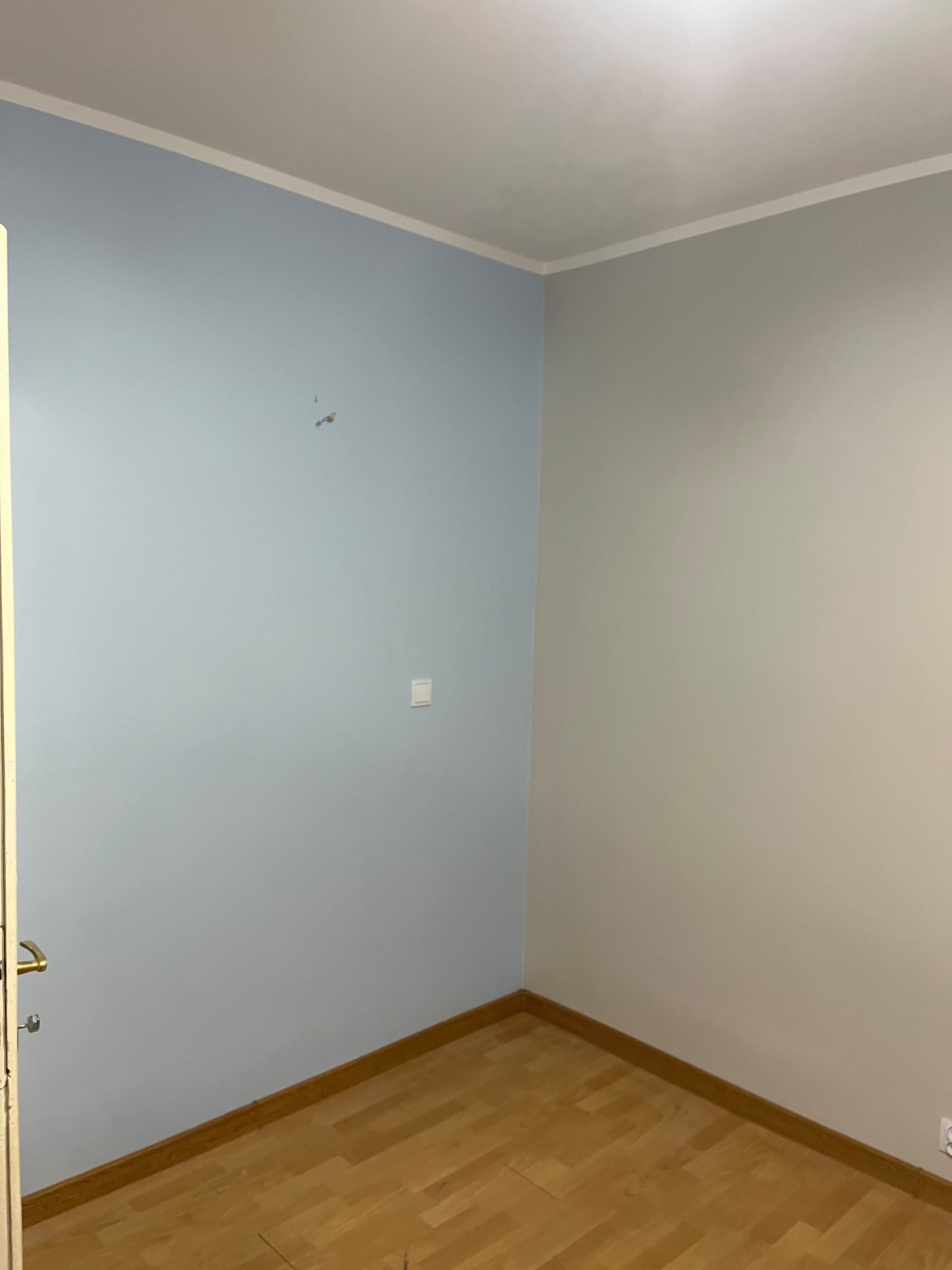 Pokój po remoncie: ściany pomalowane na dwa kolory, jasny błękit i szary, widoczny parkiet i biała listwa przypodłogowa, zarys drzwi po lewej stronie.