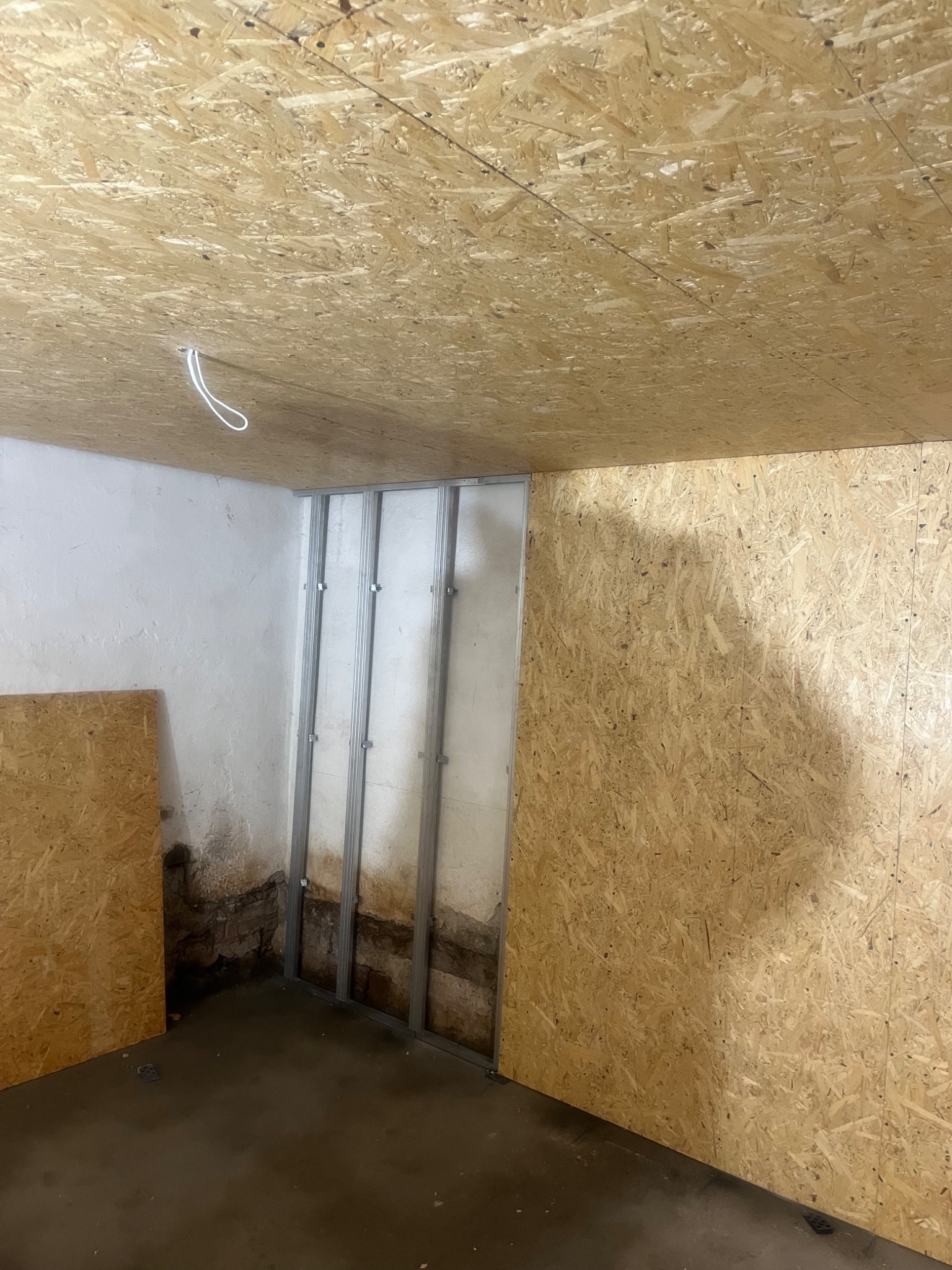 Poddasze w trakcie adaptacji: ściana z płyt OSB, metalowa konstrukcja ścianki działowej na tle starego muru z widoczną izolacją przeciwwilgociową, surowa podłoga betonowa i kabel elektryczny...