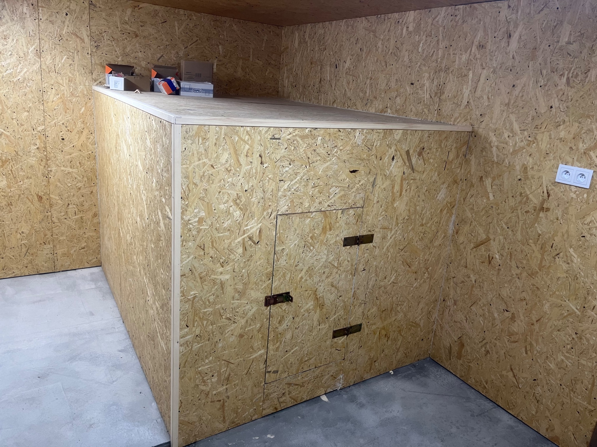 Poddasze wykończone płytami OSB, widoczna zabudowa z drzwiczkami i gniazdko elektryczne na ścianie.