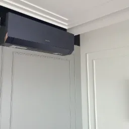 Czarny klimatyzator marki Gree zamontowany na ścianie z dekoracyjnymi panelami w jasnym wnętrzu.