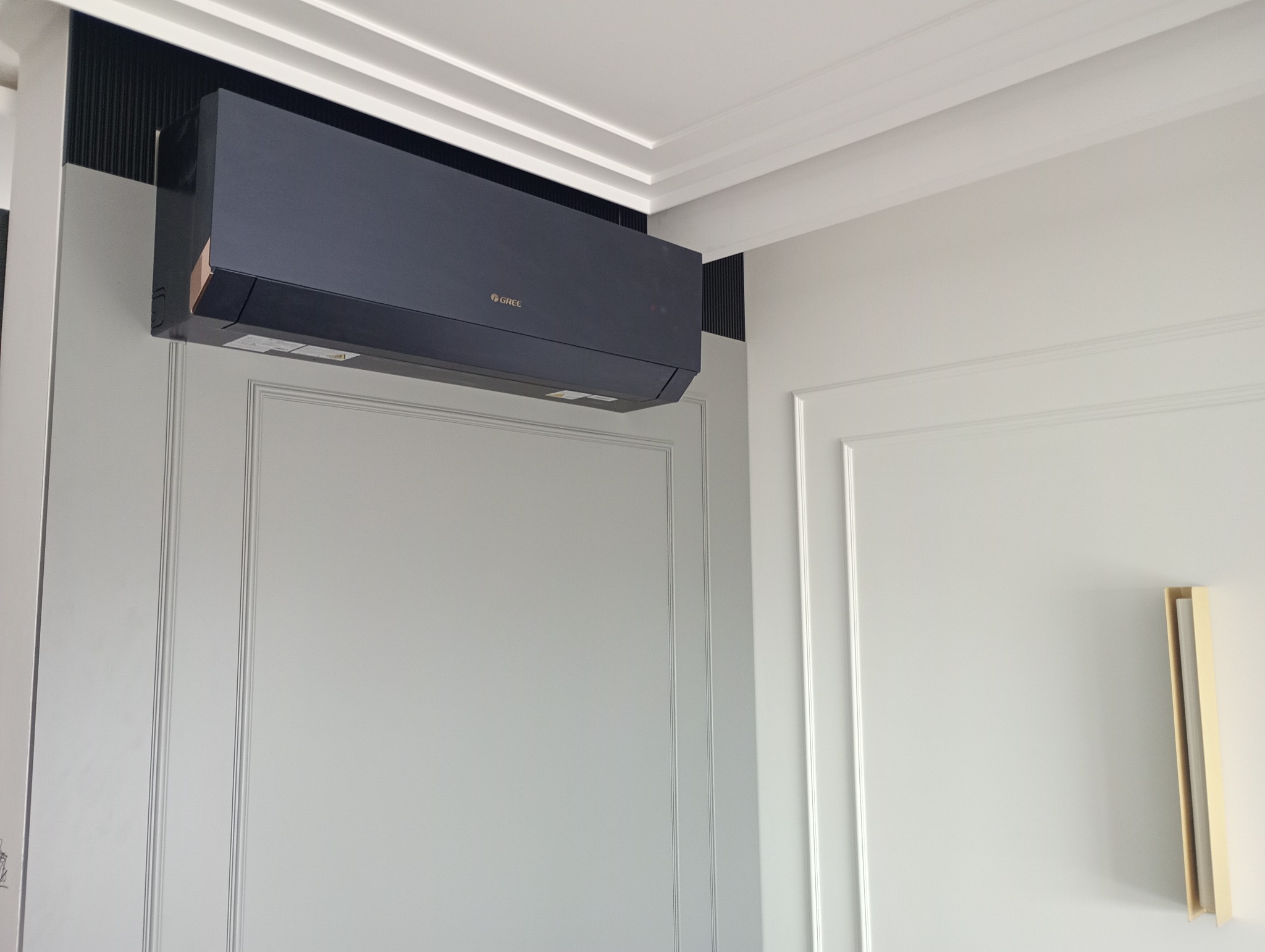 Czarny klimatyzator marki Gree zamontowany na ścianie z dekoracyjnymi panelami w jasnym wnętrzu.