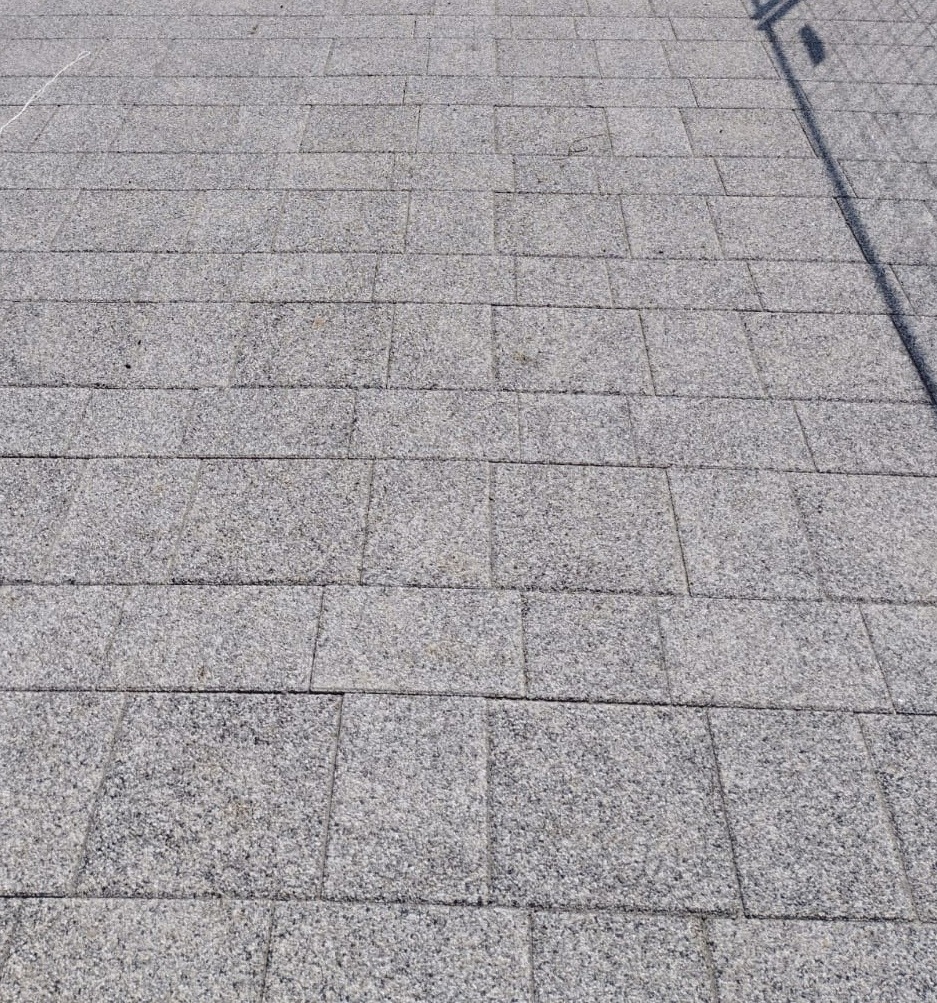 Szara kostka granitowa ułożona w regularny wzór, widoczny cień słupa w prawym górnym rogu.