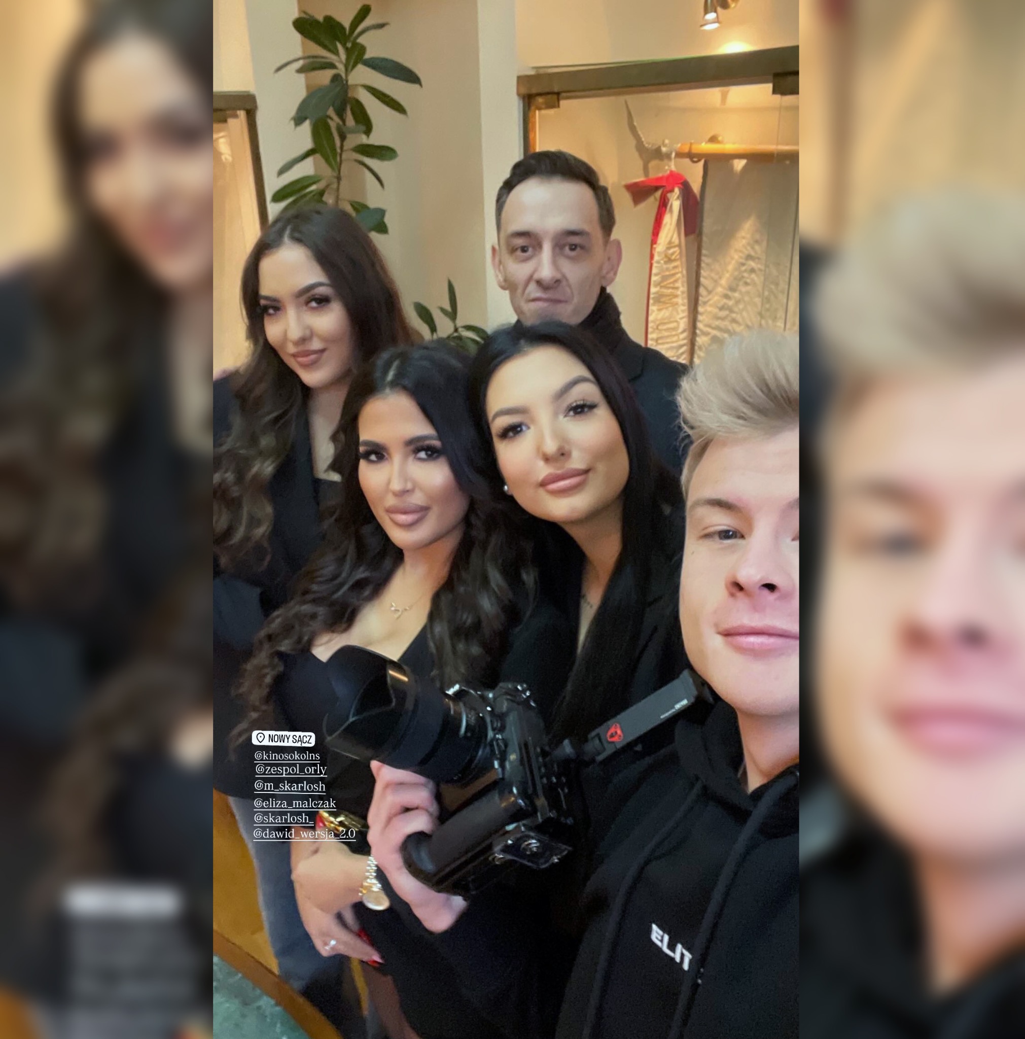 Zdjęcie grupowe z fotografem trzymającym aparat, w tle dekoracja sali i roślina doniczkowa.