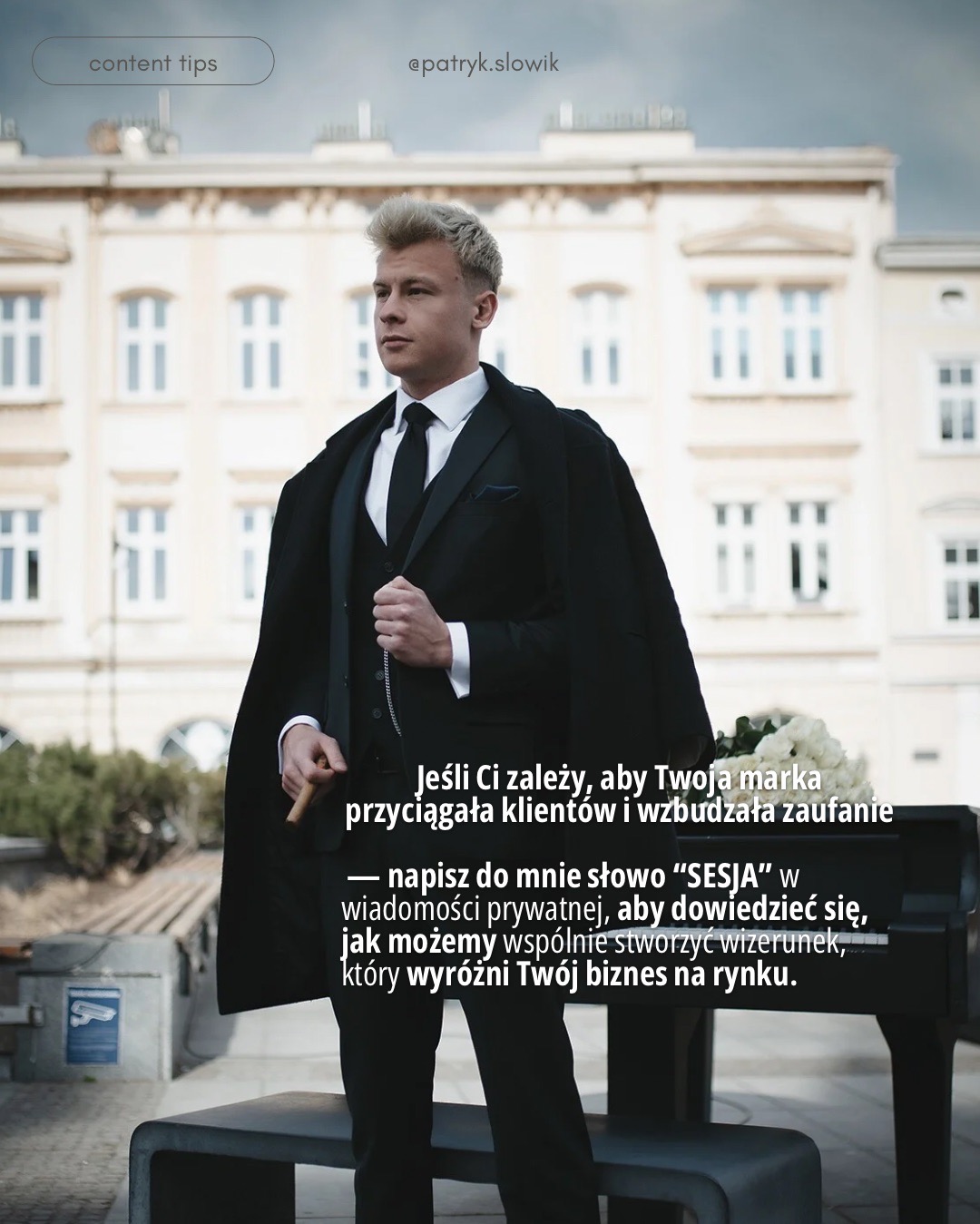 Mężczyzna w eleganckim, czarnym garniturze z kamizelką i krawatem, z narzuconym płaszczem, trzymający cygaro, pozujący na tle miejskiej architektury i kwiatów. Ujęcie podkreśla profesjonalny...