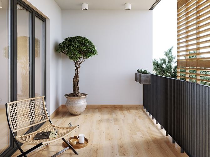 Jasny balkon z drewnianą podłogą, krzesłem z plecionki, drzewkiem bonsai w dużej donicy i czarną balustradą z drewnianymi lamelami w tle.