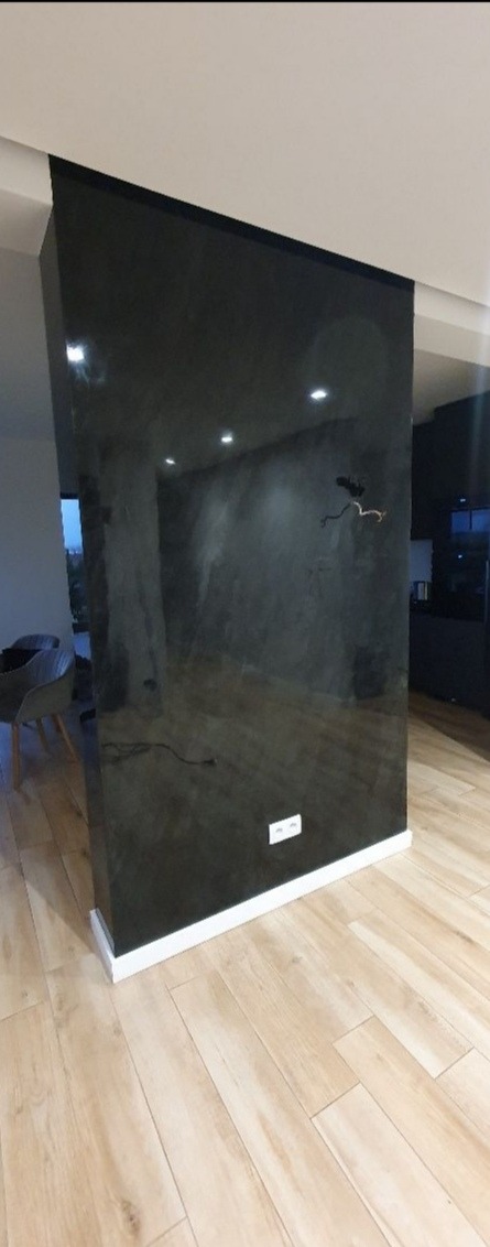 Ciemna, błyszcząca ściana działowa z dekoracyjnym wykończeniem, oświetlona punktowymi lampami sufitowymi, z widocznymi gniazdkami elektrycznymi i drewnianą podłogą w jasnym odcieniu