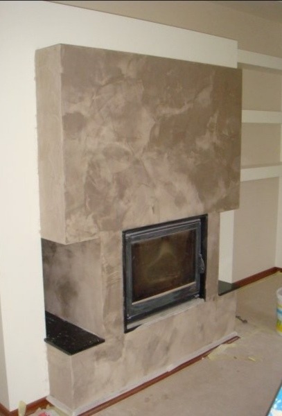 Otynkowany kominek z czarnym wkładem kominkowym w Bytomiu, z widoczną fakturą na powierzchni i czarnym blatem po lewej stronie.