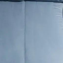 Jasnoniebieska, pluszowa kanapa z widocznym szwem pośrodku, na tle podłogi.