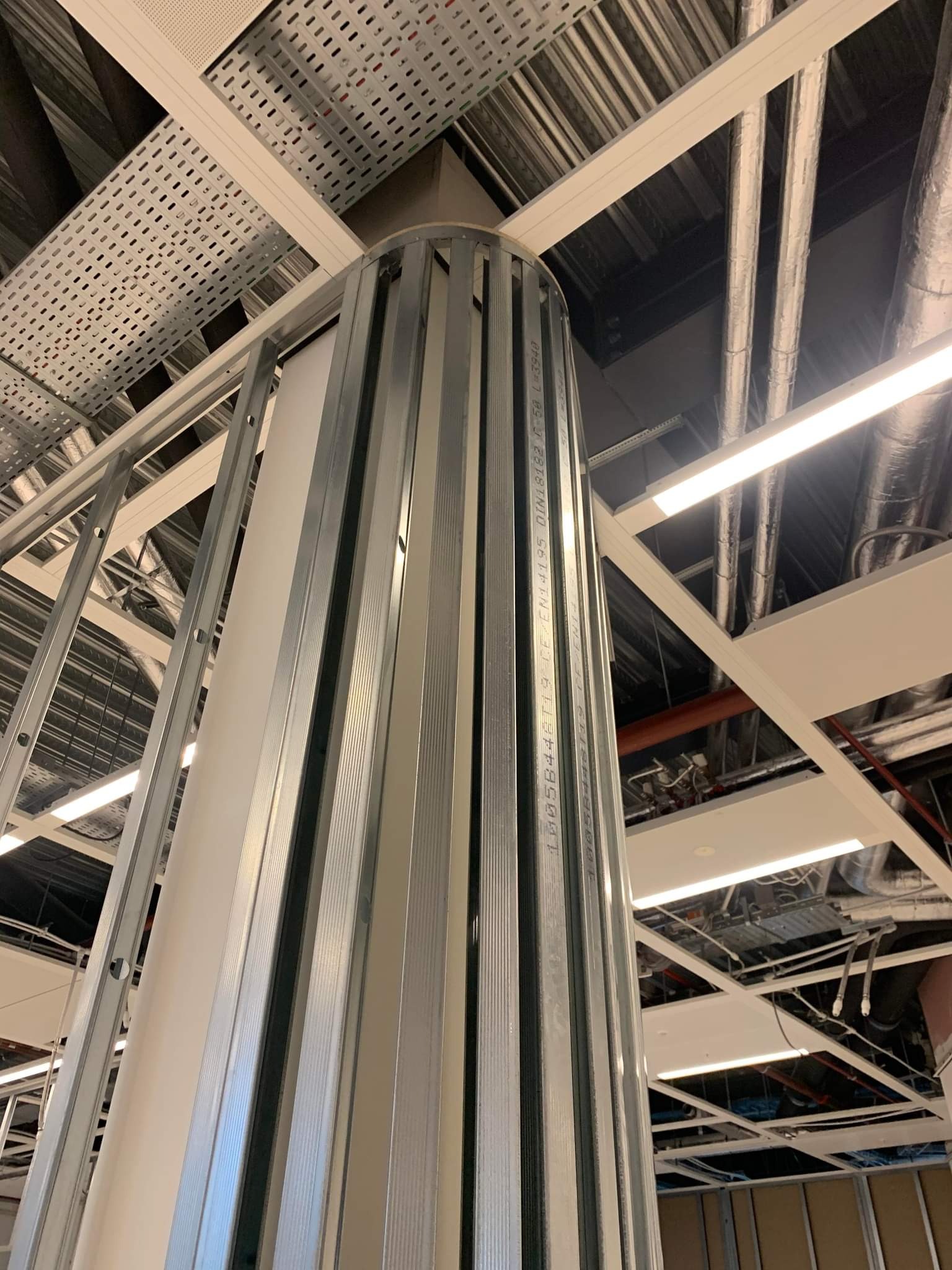 Metalowy szkielet kolumny z płyt kartonowo-gipsowych w trakcie montażu, widoczne instalacje pod sufitem podwieszanym.