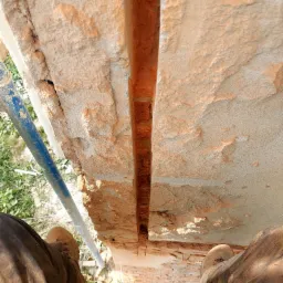 Wykonywanie pionowego nacięcia w murze z cegły, widok z góry na pracownika w ubrudzonych roboczych spodniach i butach stojącego na rusztowaniu.