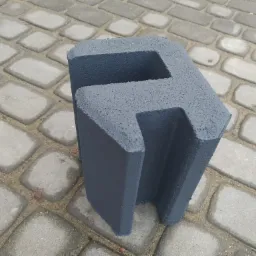 Szary, betonowy element ogrodzeniowy w kształcie litery 'E' ustawiony na kostce brukowej.