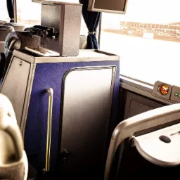 Wnętrze autobusu dalekobieżnego z widocznymi fotelami, stolikiem, zasłoną w oknie i automatem do napoj&oacute;w.