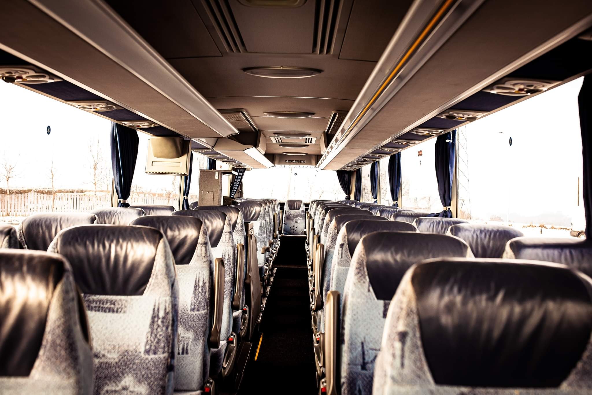 Wnętrze autobusu dalekobieżnego w Choczni z rzędami foteli obitych wzorzystą tkaniną i czarną skórą, widok z perspektywy pasażera w kierunku przedniej szyby.