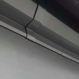 Szare panele blaszane trapezowe z widocznym łączeniem, ujęcie z dołu, z fragmentem podłoża w dolnej części kadru.