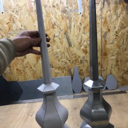 Hexagon Hub - Dwa metalowe elementy dekoracyjne w kształcie wieżyczek, jeden surowy, drugi polerowany, na tle drewnianej płyty OSB.