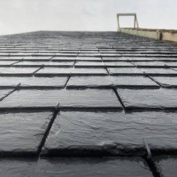 Hexagon Hub - Świeżo położone, mokre, czarne dachówki łupkowe pod kątem, widoczne elementy konstrukcji dachu w tle.