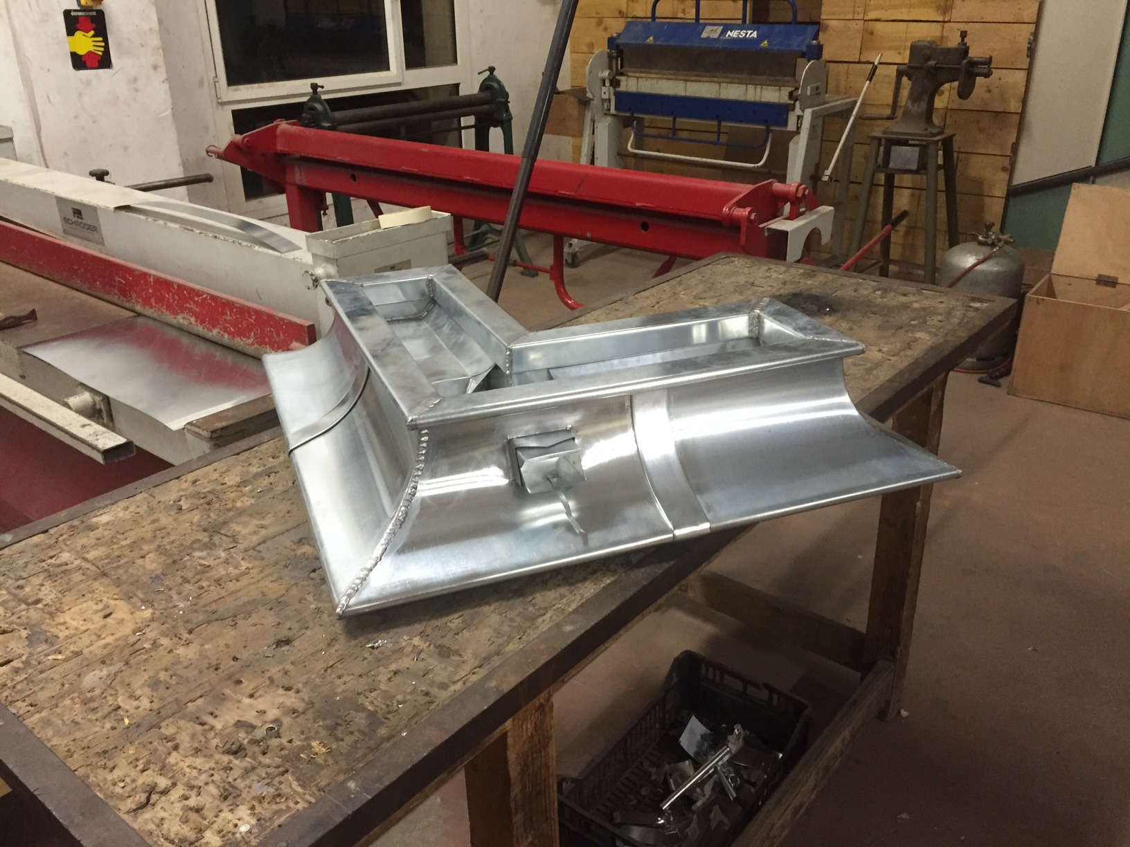 Kątowa rynna dachowa z blachy aluminiowej, spawana, leżąca na drewnianym stole warsztatowym, w tle maszyny do obróbki blach.