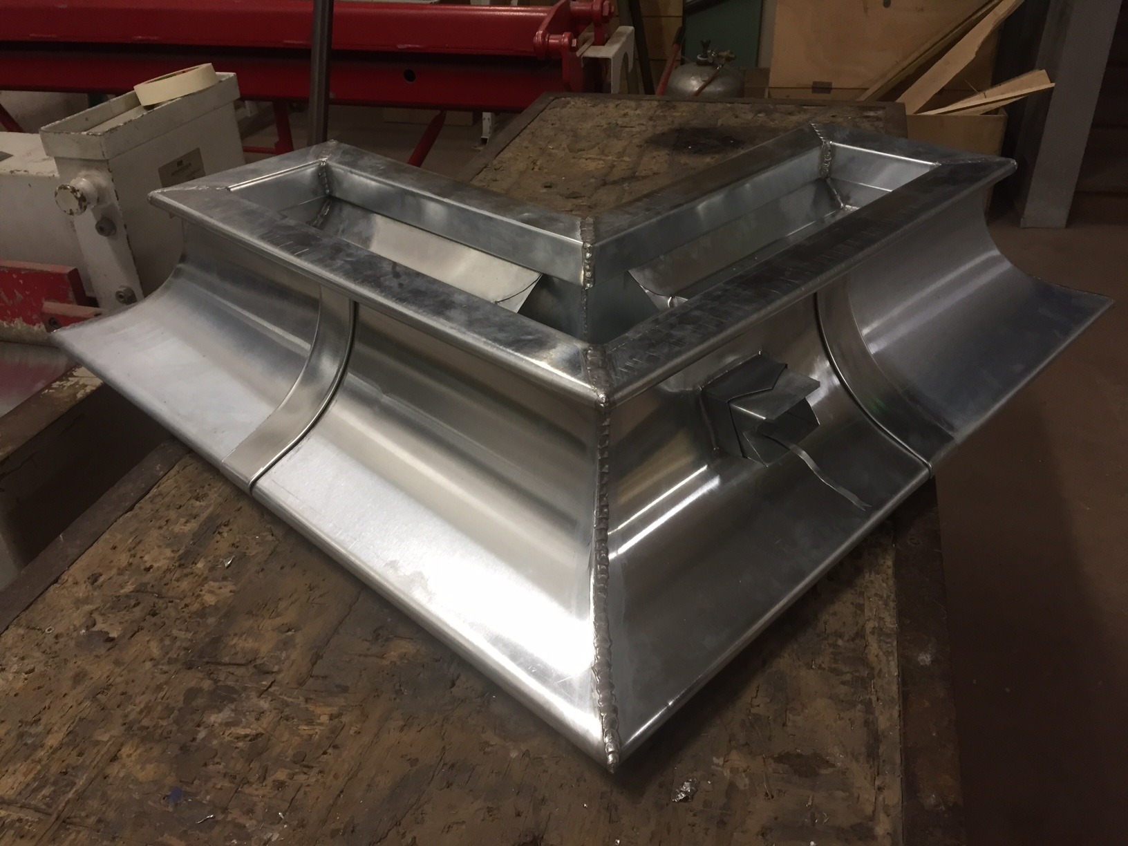 Kątowa, metalowa rynna dachowa w kształcie litery L, z widocznymi spawami i mocowaniami, leżąca na drewnianym stole warsztatowym.