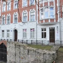 Elewacja kamienicy z biurem nieruchomości, widoczne tabliczki informacyjne i ogłoszenia w oknach