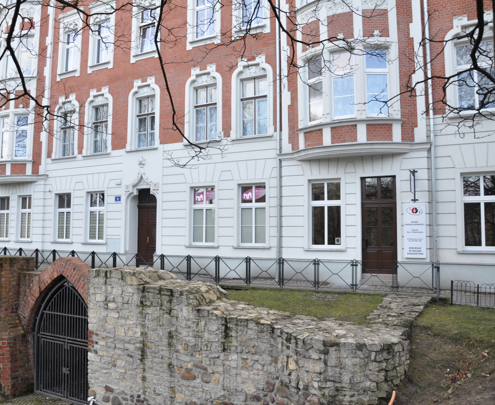 Elewacja kamienicy z biurem nieruchomości, widoczne tabliczki informacyjne i ogłoszenia w oknach