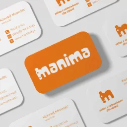 Wizytówki firmy Manima, sklepu z zabawkami dla dzieci, z pomarańczowym logo i danymi kontaktowymi Konrada Mrowca, właściciela, ułożone na jasnym tle pod kątem.