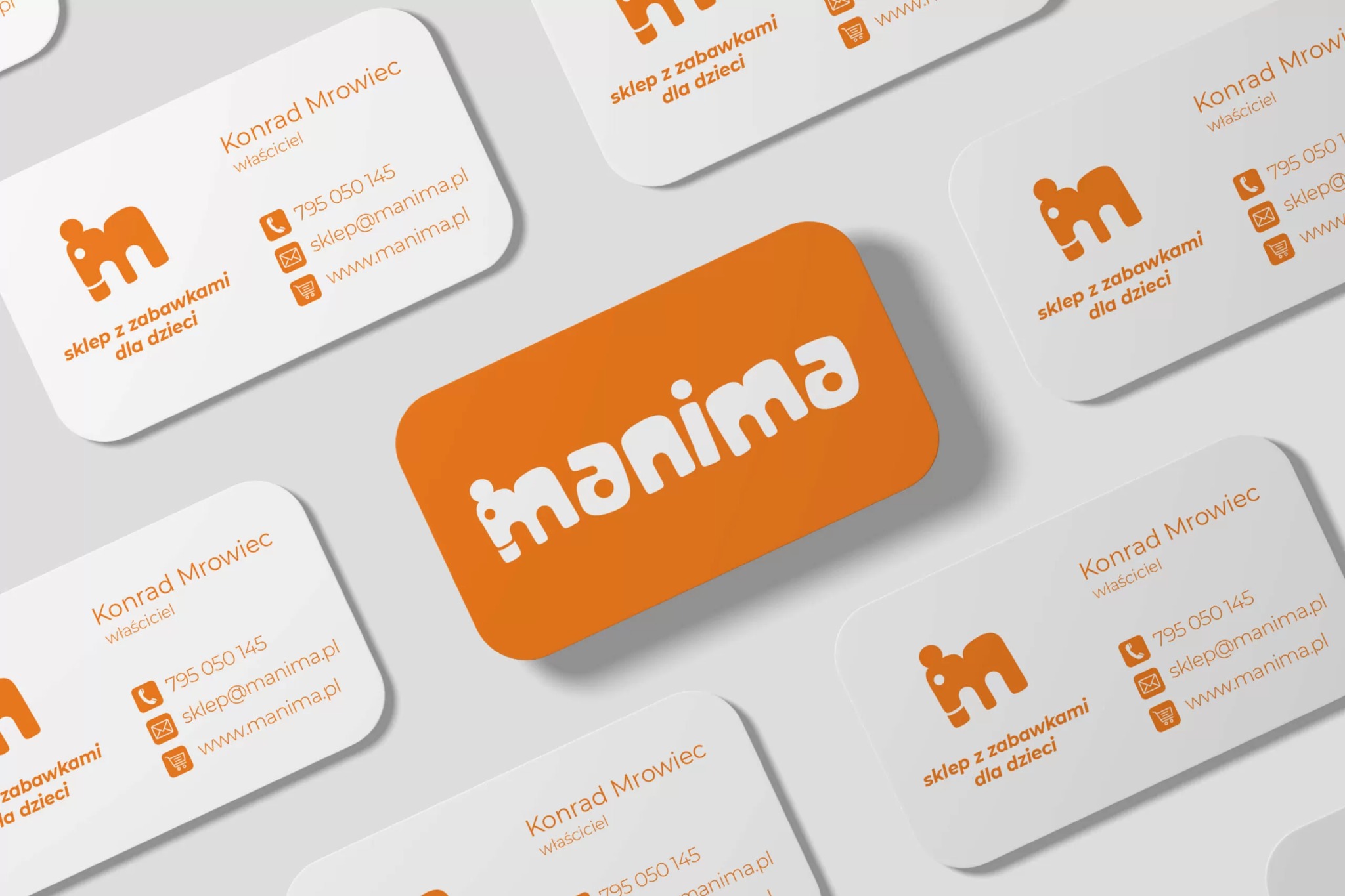 Wizytówki firmy Manima, sklepu z zabawkami dla dzieci, z pomarańczowym logo i danymi kontaktowymi Konrada Mrowca, właściciela, ułożone na jasnym tle pod kątem.