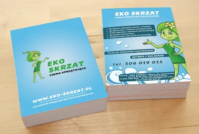 Stos wizytówek firmy sprzątającej Eko Skrzat z zieloną postacią i informacjami kontaktowymi na jasnoniebieskim tle.