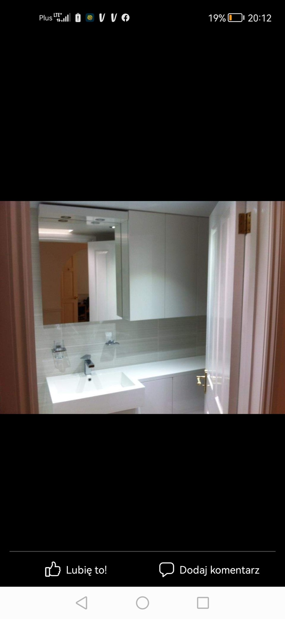 Nowoczesna łazienka z prostokątną umywalką nablatową, szarą glazurą i białymi szafkami, widok zza uchylonych drzwi.