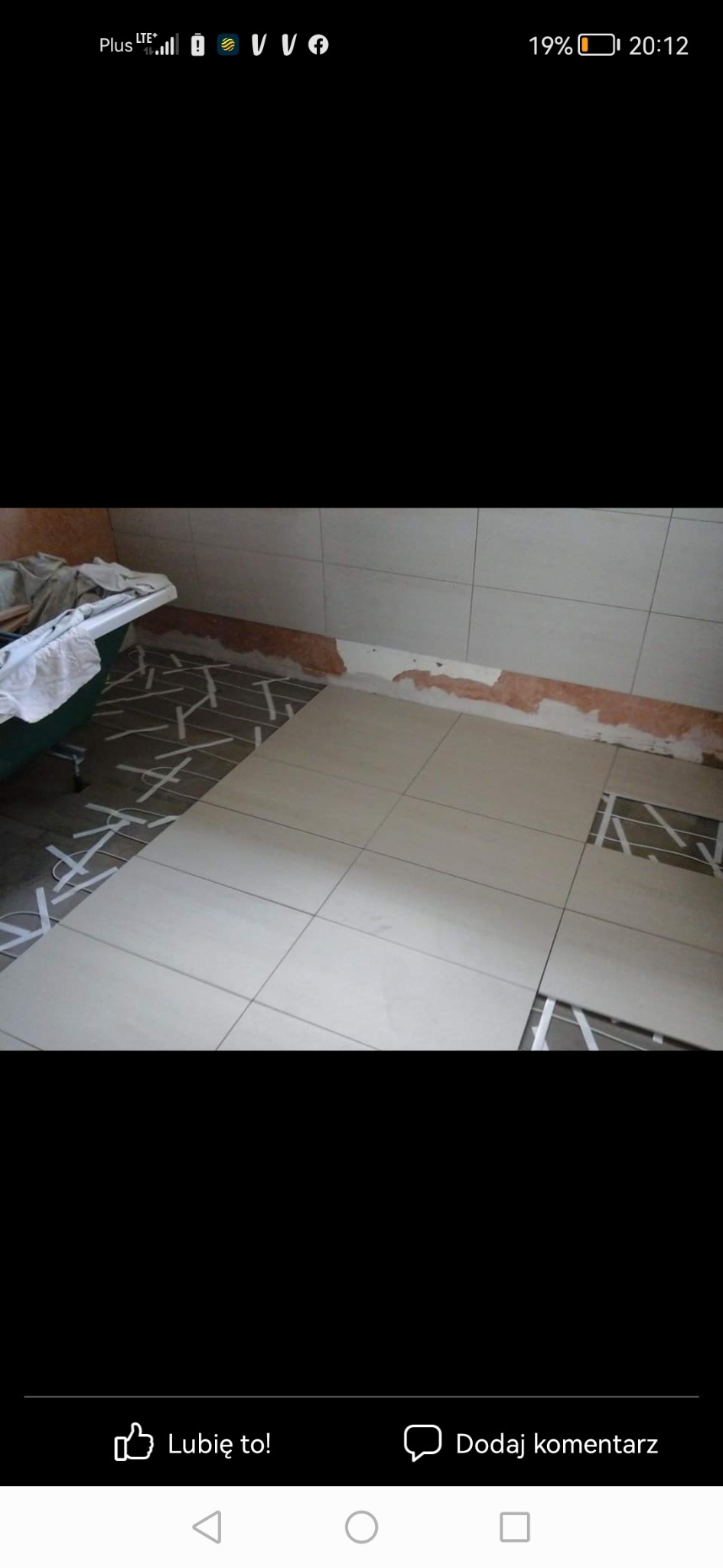 Układanie jasnych, kwadratowych płytek podłogowych w łazience, widoczne listwy dystansowe i fragment wanny z praniem.